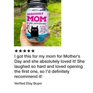 Puede incluir: Un frasco de vidrio transparente con tapa negra que contiene papeles de colores. La etiqueta muestra una ilustraci&oacute;n de un gato negro con flores y el texto: SERIOUSLY MOM no joke. you're the shit! 48 reasons why you mean the eff'in World to Me.