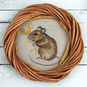May include: A brown wicker frame with a beige fabric insert featuring an embroidered image of a brown mouse holding a stalk of wheat.