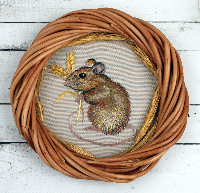 May include: A brown wicker frame with a beige fabric insert featuring an embroidered image of a brown mouse holding a stalk of wheat.