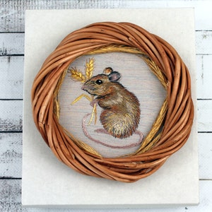 May include: A brown wicker wreath with a beige fabric center featuring an embroidered image of a brown mouse holding a stalk of wheat.
