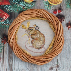 May include: A brown wicker wreath with a white fabric circle in the center. The fabric circle has an embroidered image of a brown mouse holding a stalk of wheat.