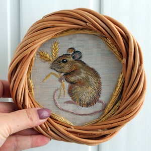 May include: A brown wicker frame with a beige fabric insert featuring an embroidered image of a brown mouse with a long tail and a sprig of wheat.