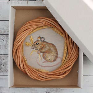May include: A brown wicker circle with a beige fabric center featuring an embroidered image of a brown mouse holding a stalk of wheat.