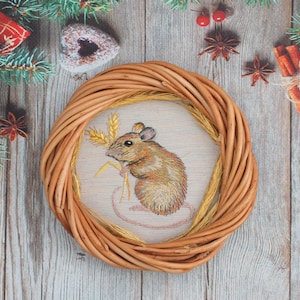 May include: A brown wicker wreath with a beige fabric center featuring an embroidered image of a brown mouse holding a stalk of wheat.