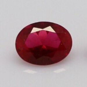 Puede incluir: Una piedra preciosa de color rojo intenso y forma ovalada con una superficie facetada. La piedra muestra un tono carmesí vibrante y saturado, con múltiples facetas triangulares y trapezoidales que reflejan la luz, creando un aspecto pulido.
