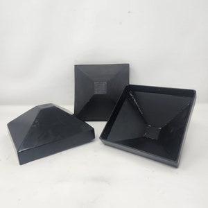 May include: Three black metal pyramid-shaped fence post caps. The caps are designed to fit over the top of a square fence post.