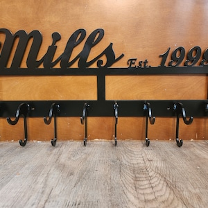 May include: Black metal coat rack with the name "Mills Est. 1999" and eight hooks.