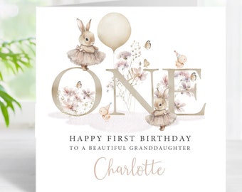May include: A white card with a watercolour illustration of the number "ONE" decorated with flowers and butterflies. Two bunnies wearing pink tutus are standing on the number. The text "Happy First Birthday to a beautiful granddaughter Charlotte" is printed below the number.