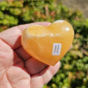 May include: A heart-shaped orange calcite crystal with a white label that reads "Made in Mexico".