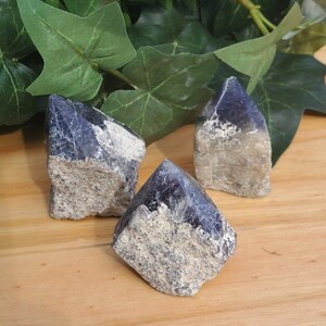 May include: Three dark blue and grey crystal points, also known as amethyst, on a wooden surface.