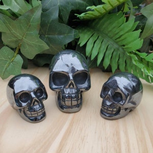 May include: Three black hematite skull sculptures of varying sizes. The skulls are carved with detailed facial features and are polished to a smooth finish.