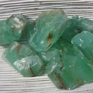 May include: A group of green calcite crystals with brown inclusions. The crystals are rough and have a translucent appearance.