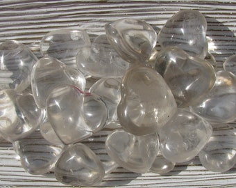 May include: A collection of clear quartz heart-shaped crystals on a white wooden surface.
