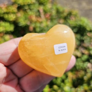 May include: A heart-shaped, polished, yellow calcite crystal. The crystal is smooth and has a light yellow color. The label on the crystal reads "MADE IN MEXICO".