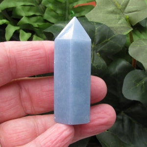 May include: A light blue crystal point, also known as a crystal wand, is shown in the image. The crystal point is smooth and polished, with a pointed tip and a flat base. The crystal point is approximately 2 inches in length.