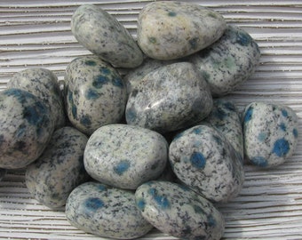 May include: A collection of smooth, polished K2 stones. These stones are primarily white with speckled gray and blue spots. The stones are oval-shaped and vary in size, creating a natural, organic aesthetic.