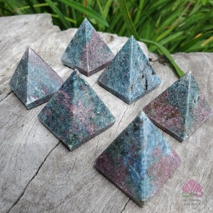 May include: Six green and pink ruby zoisite pyramids on a wooden surface. The pyramids are all the same size and shape, and they are arranged in a semi-circle.