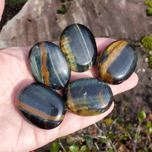 May include: Five smooth, polished blue tiger's eye stones with golden bands. The stones are oval shaped and have a glossy finish.