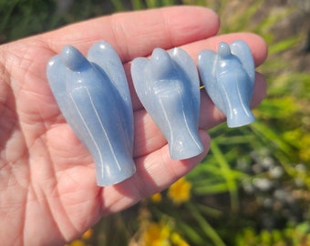 May include: Three blue angel figurines carved from a light blue crystal. The figurines are arranged in a row from largest to smallest, with the largest figurine on the left and the smallest figurine on the right.