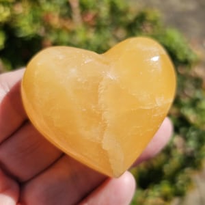 May include: A heart-shaped, polished, yellow calcite crystal. The crystal has a smooth, polished surface and a light yellow color.
