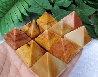 May include: A collection of nine yellow, orange, and red gemstone pyramids. The pyramids are all different sizes and shapes, and they are arranged in a random pattern.