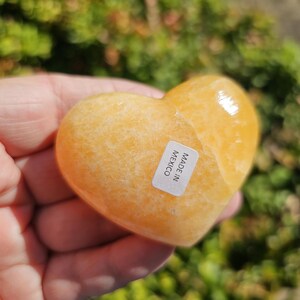 May include: A heart-shaped, polished, orange calcite crystal. The crystal is smooth and has a label that reads "Made in Mexico".