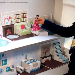 May include: A paper dollhouse with a blue and white bedroom, a living room with a fireplace, a dining room with a table and chairs, and a staircase. The dollhouse is made of cardboard and has a pop-up design. A girl is playing with the dollhouse and holding a paper doll.