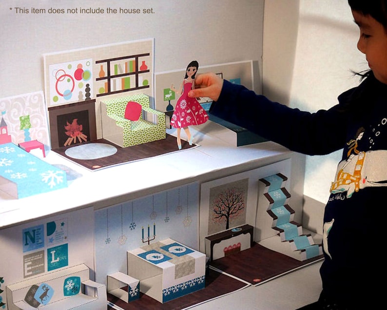 May include: A paper dollhouse with a blue and white bedroom, a living room with a fireplace, a dining room with a table and chairs, and a staircase. The dollhouse is made of cardboard and has a pop-up design. A girl is playing with the dollhouse and holding a paper doll.