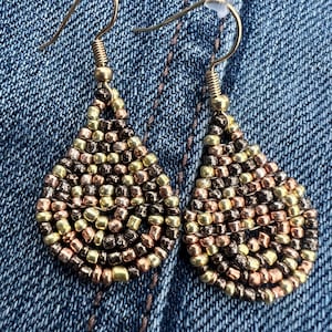 May include: A pair of teardrop-shaped earrings made with small gold, copper, and brown beads. The earrings have a simple gold hook closure.