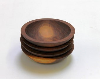 May include: Four wooden bowls stacked on top of each other. The bowls are made of dark brown wood and have a smooth, polished finish.