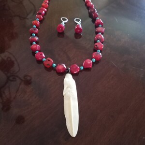 May include: A red coral necklace with turquoise accents and a white bone pendant. The necklace is paired with matching earrings.