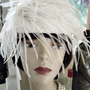 May include: A white feather hat with a pearl necklace. The hat is made of white feathers and has a wide brim. The necklace is made of white pearls and is worn around the neck.