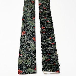 May include: Two fabric items with a dark green background, adorned with green leaves, red berries, and gold glitter. One item is a tie, and the other is a gathered sleeve. The items are likely Christmas-themed.
