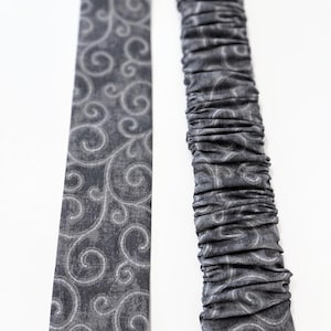 May include: Two pieces of gray fabric with a white swirl pattern. One piece is flat and the other is gathered.