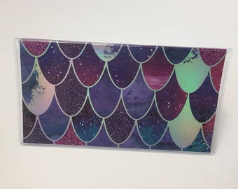 May include: A clear plastic envelope with a mermaid scale pattern. The scales are iridescent and have a purple, blue, and green color scheme.