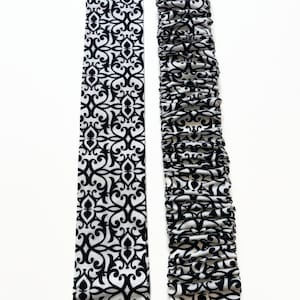 May include: Two black and white patterned fabric strips. One strip is flat and the other is gathered.