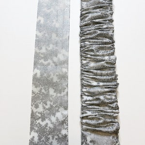May include: Two pieces of white fabric with a silver snowflake pattern. One piece is flat and the other is gathered.