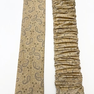 May include: Two fabric strips with a paisley pattern in shades of brown and beige. One strip is flat and the other is gathered.