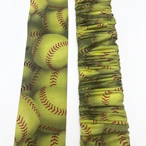 May include: Two fabric arm warmers with a green and yellow softball pattern. One arm warmer is flat and the other is gathered.