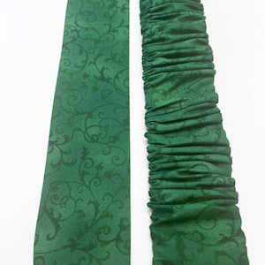 May include: Two green fabric pieces with a dark floral pattern. One piece is flat, the other is gathered. The fabric is a deep emerald green color. The pattern is a darker shade of green.