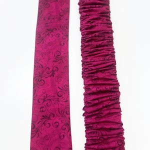 May include: A pink fabric with a black floral pattern. The fabric is shown flat and gathered.