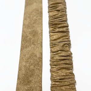 May include: A brown fabric ribbon with a white floral pattern. The ribbon is gathered on one side, creating a ruffled effect.