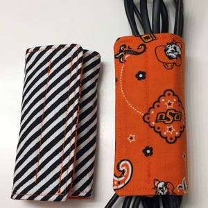 May include: Two fabric cord organizers. One is black and white striped and the other is orange with a paisley pattern and the letters "OSU".