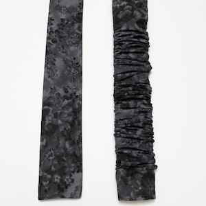 May include: Two black fabric strips with a floral pattern. One strip is flat and the other is gathered.