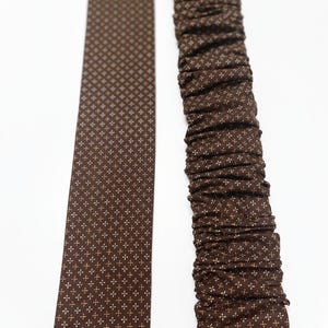 May include: A brown fabric ribbon with a white and brown geometric pattern. The ribbon is shown flat and gathered.