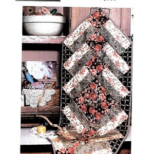 May include: A quilting pattern for a table runner with a floral design. The pattern is called "Fat Quarter Table Runner II" and is labeled with the number "#Q111". The pattern is from "Out Of The Blue" and is a quilt-as-you-sew project.