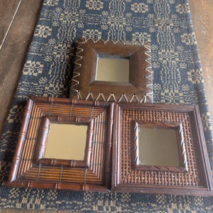 May include: Three square wall mirrors with distinct frames. The top mirror has a smooth brown leather-like border with white stitching. The bottom left mirror features a bamboo-style frame, and the bottom right mirror has a woven rattan border.