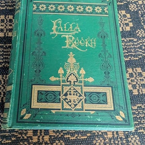 May include: A vintage book with a green cover and gold lettering. The title "Falla Books" is prominently displayed. The cover features ornate gold designs and decorative borders, giving it an antique aesthetic.