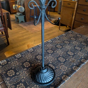 May include: A matte black metal mug tree stand featuring a circular base with a ribbed, scalloped design. The central vertical post is topped with a decorative finial and includes four curved hooks extending outward to hold mugs or other items.