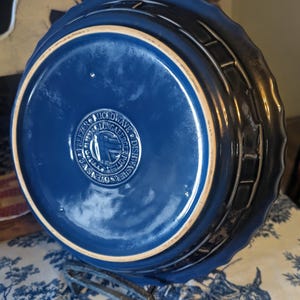 May include: A deep blue ceramic pie dish with a scalloped edge. The underside features a circular stamp with the text Longaberger Pottery, Made in U.S.A., Microwave, Dishwasher, Oven Safe, and Freezer Safe, centered on the smooth glazed base.